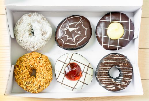 Color donuts in box on the white wood table from top view.