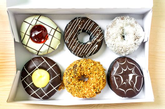 Color donuts in box on the white wood table from top view.