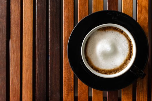 A Cup of Cappuccino Coffee on the horaizontal line brown wood table and ready to served and enjoy drink in the relaxing time with copy space.