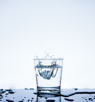 Ice with water splashing in the glass with reflection on mirror.