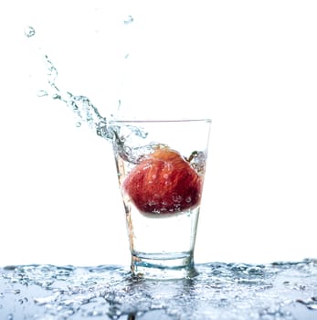 Red apple has droping to the glass and splashing water around the glass and on the table with reflection and isolated white background.