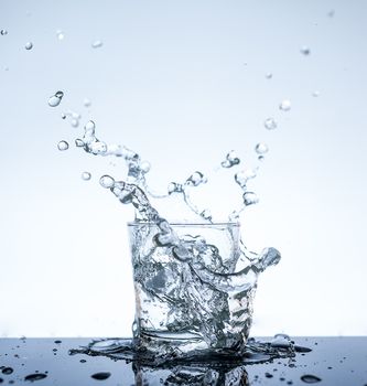 Water splashing in the glass with reflection on mirror.