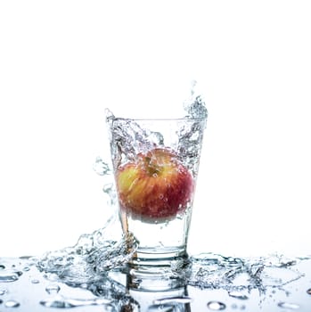Red apple has droping to the glass and splashing water around the glass and on the table with reflection and isolated white background.