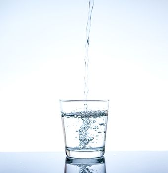 Pouring water and splashing in the glass with reflection on mirror.