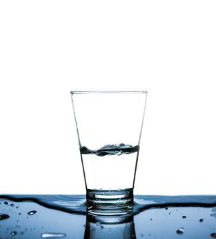 Glass of water was drinking for half a glass of water and splashing on the table with reflection.