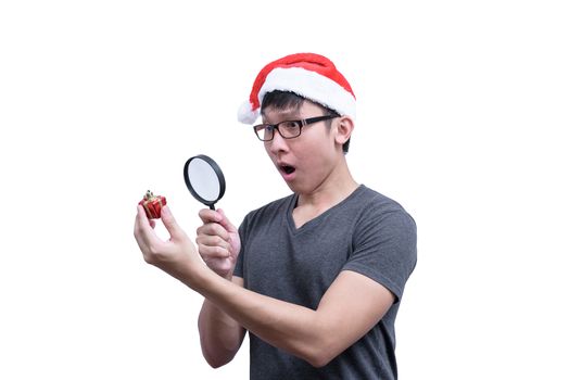 Asian Santa Claus man with eyeglasses and grey shirt has searching and looking a red gift box with magnifying glass isolated on white background with copy space.