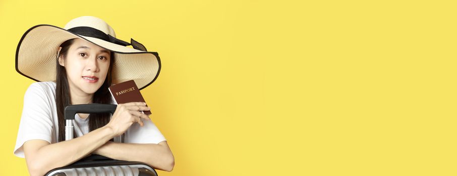 Asian women long hair wear Straw hat with black ribbon in hand holding passport book and travel bag with copy space banner. Young girl ready to travel with suitcase and passport on yellow background. Summer travel concept.