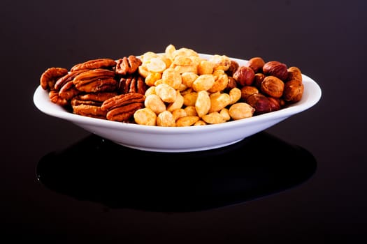 Assorted nuts (Pecan, Hazelnuts and Roasted Salted Peanuts) in a white plate on a black background