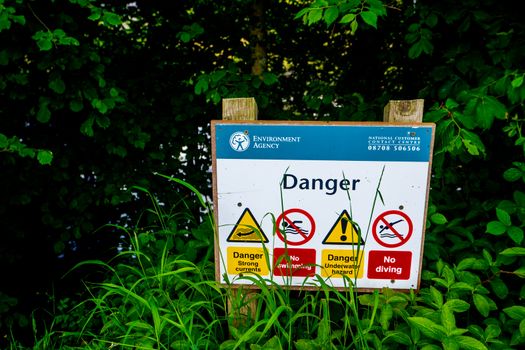 Danger no diving or swiming sign on the wooden pole in hedge