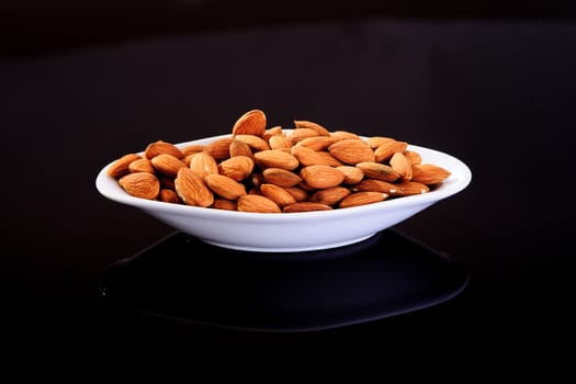 Raw Almonds in a white plate on a black background