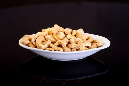 Raw Cashew Nuts in a white plate on a black background