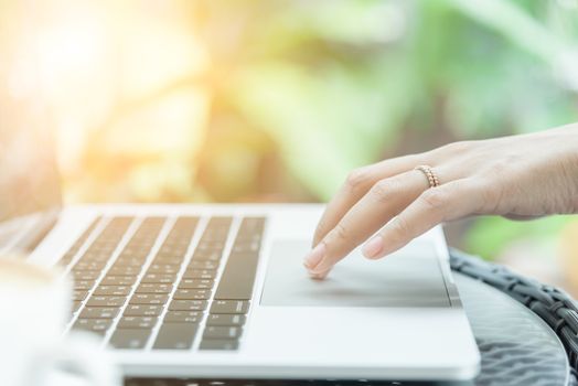 Asian woman hands and married ring has touching and typing on laptop computer with blurred coffee, computer and view outside window.