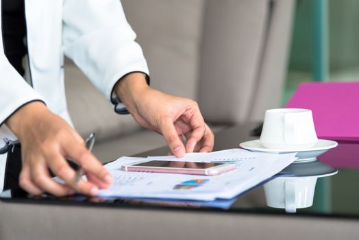 Hand of businesswoman holding with silver pen and playing a phone on documents in the office interrior