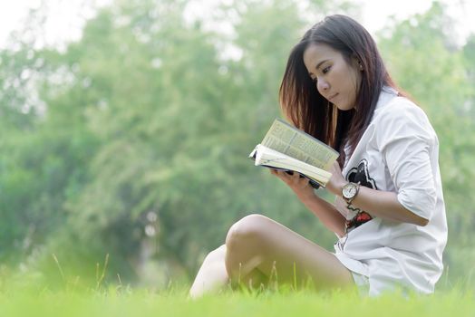 Beautiful asian woman reading a book at garden with happiness and relaxing in the evening with sunset time.