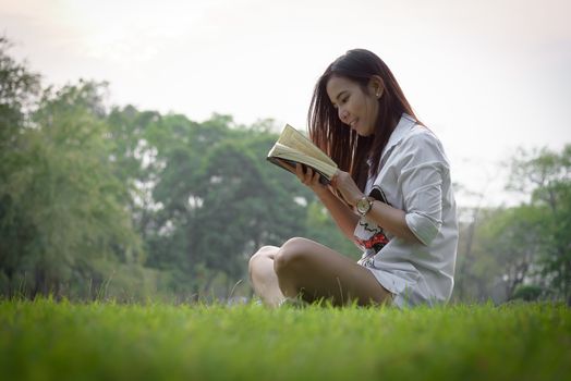 Beautiful asian woman reading a book at garden with happiness and relaxing in the evening with sunset time.