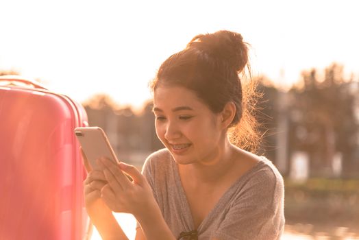 A beautiful tourist woman with big bag has playing phone in the evening with sunset time at garden park and river.