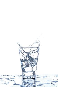 Ice dropping and water splashing in the glass with reflection on the mirror table and isolated on white background.