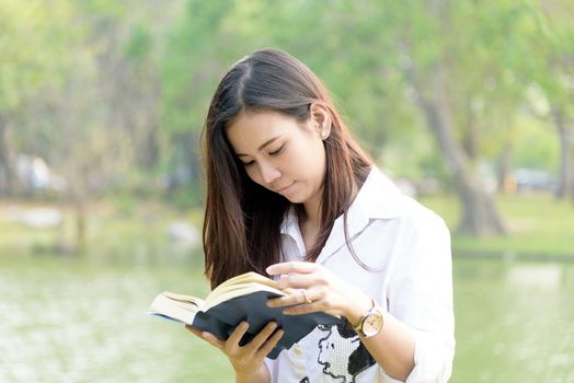 Beautiful asian woman reading a book at garden with happiness and relaxing in the evening with sunset time.