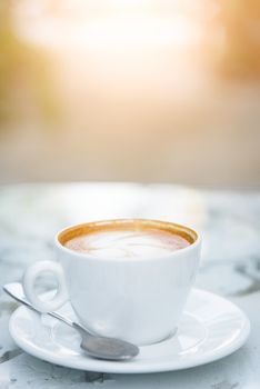 A white cup of coffee and silver spoon ready to served in the morning with relaxing and yellow lighting bokeh background.