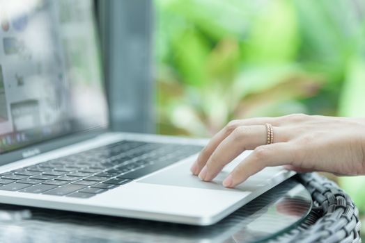 Asian woman hands and married ring has touching and typing on laptop computer with blurred coffee, computer and view outside window.