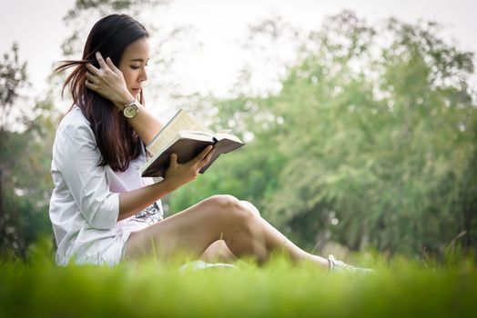 Beautiful asian woman reading a book at garden with happiness and relaxing in the evening with sunset time.