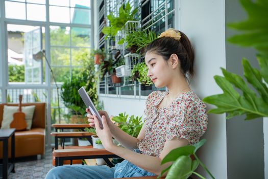 Asian woman is using digital tablet for read news and shopping online in the garden at home in relaxing time