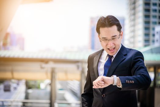 The asian businessman has holding a black bag and looking on watch in hurrying time.