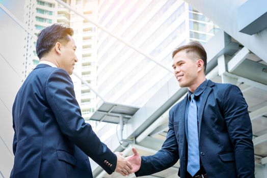 Two asian business have handshake with building and city background.