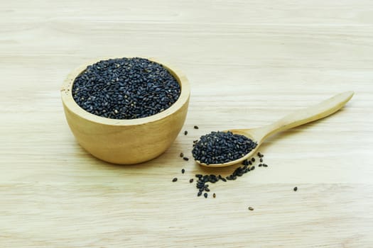 Black sesame seeds in wooden spoon pile on wood table 