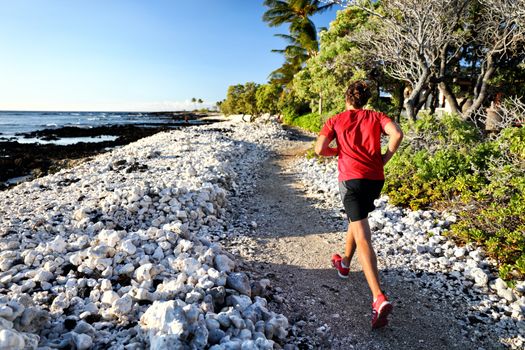 Trail runner jogging on running path at beach in white coral rocks at hawaii travel destination. Male athlete from behind doing cardio exercise outdoors in nature.