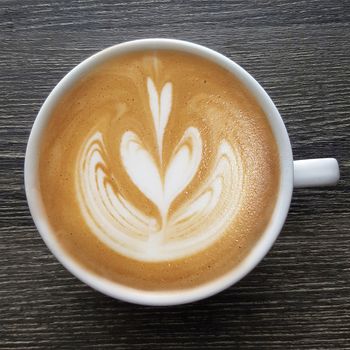 Top view of a mug of latte art coffee on timber background.