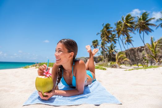 Happy girl lying down sun tanning on beach vacation. Asian woman relaxing sunbathing drinking fresh coconut water. Tropical travel destination, Suntan in summer holiday.