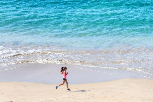 Woman runner training cardio running by the ocean on the beach. Morning workout. Copyspace on blue water.