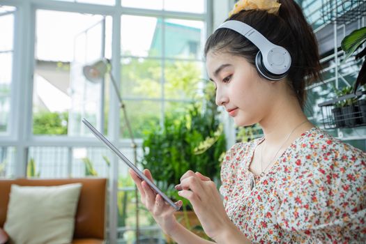 Asian women wearing headphones and using mobile phone and digital tablet for Listening to music and singing on a relaxing day at home