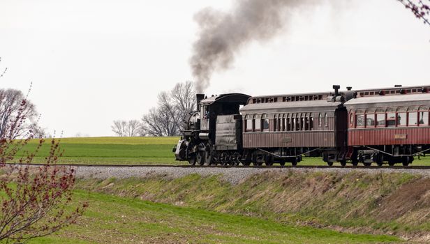 A beautiful shot of an antique steam train and passenger cars, puffing smoke thru countryside