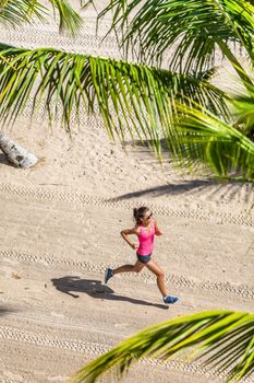 Healthy active life sport woman running training cardio on tropical beach in between palm trees. View from above. Health and fitness concept.
