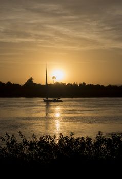 Traditional egyptian felluca sailing boat on river Nile in silhouette at dusk sunset