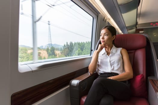 Woman relaxing enjoying view during morning commute. Business class seat in train. Asian businesswoman pensive looking out the window in travel transport.