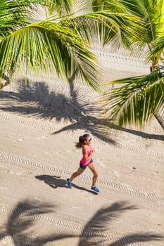 Healthy active lifestyle sport woman running doing exercise workout on tropical beach in between palm trees. View from above of the ground and sand. Health and fitness concept.
