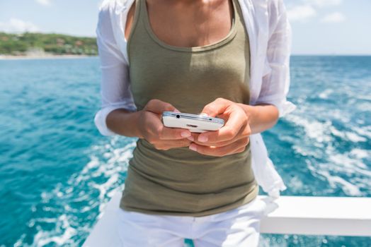 Tourist using smartphone mobile app to text sms while traveling on cruise ship tour. Woman holding phone texting on boat ride during travel summer vacation.
