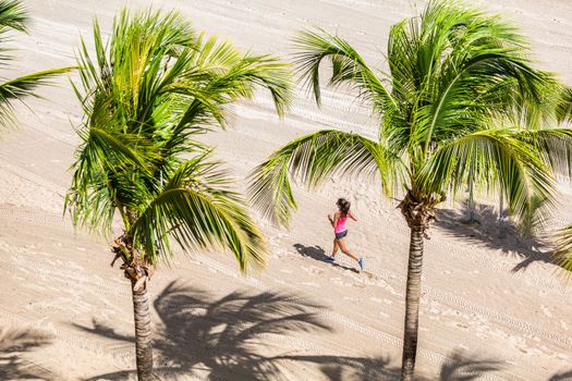 Fitness woman running training on tropical beach in between palm trees. View from high angle, hero shot. Health and sports concept. Copyspace.