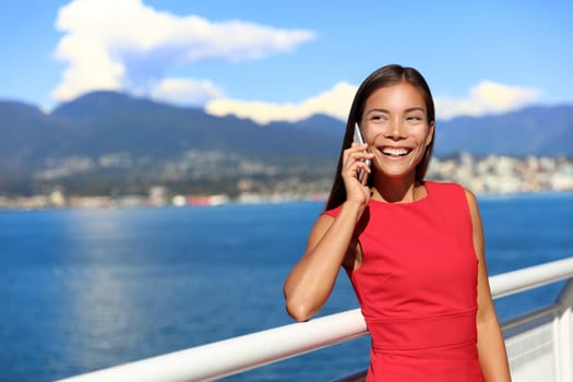 Happy asian woman talking on the phone in vancouver city harbour on summer day. Beautiful landscape of canadian nature river and mountains. Businesswoman on smartphone lifestyle.