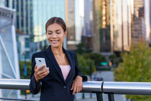 Woman sms texting using app on smart phone in city business district. Young business woman using smartphone smiling happy wearing suit jacket outdoors. Urban female professional in her 20s.