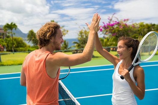 Fitness sport tennis couple giving high five energetic after fun mixed double game. Tennis players friends having fun doing fit sport at hotel ,summer travel vacation. Asian woman, Caucasian man.