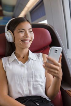 Modern people city lifestyle. Young urban woman using phone app and wireless headphones to listen to music or audiobooks online. Asian girl enjoying train travel in business class seat.