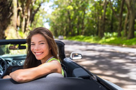 Happy young Asian woman relaxing in convertible car on summer road trip vacation. Travel destination driving through nature roads.