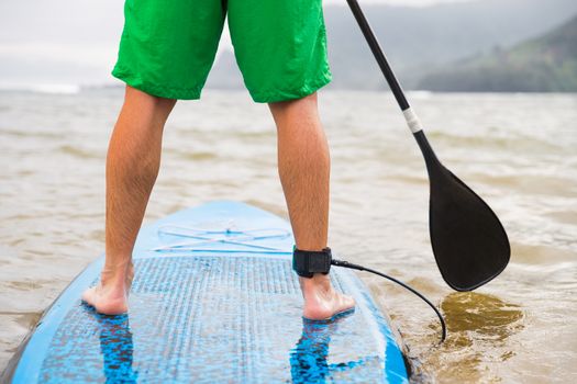 Paddleboard man paddling on SUP stand up paddle board on lake. Closeup of feet and legs.