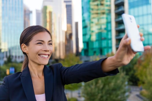 Business woman taking selfie photo using smart phone app on smartphone for social media. Young businesswoman using smartphone smiling happy. Vancouver, Canada outdoors. Urban female professional.