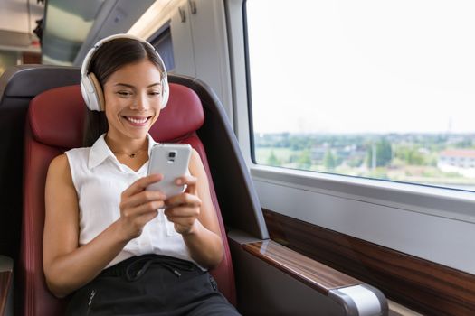 Modern people city lifestyle. Young urban woman using phone app and wireless headphones to listen to music or play video games online. Asian girl enjoying train travel in business class seat.