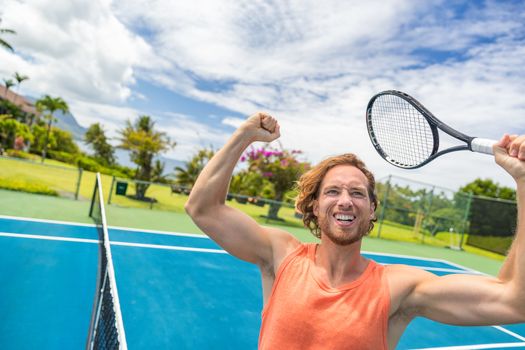 Tennis player man winning cheering celebrating victory. Winner man happy in celebration of success and win. Fit male athlete on tennis court outdoors holding tennis racket in triumph by the net.